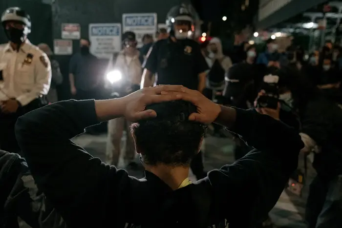 A protester has their hands on their head, as seen from behind, with officers in the background